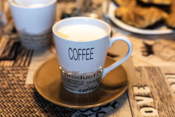 Dekoratif harflerle dolu bir kahve fincanı ve seçici odaklı bir masanın üzerinde çikolatalı çörekler. - Fotoğraf, Görsel