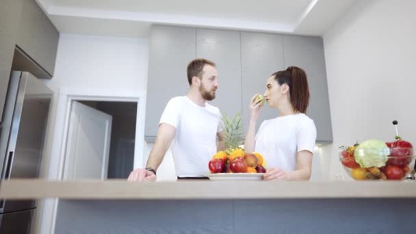 Νεαρό χαρούμενο ζευγάρι στην κουζίνα συζητώντας φρούτα και λαχανικά - Πλάνα, βίντεο