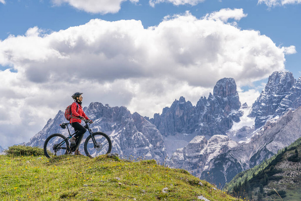 mukava ja aktiivinen vanhempi nainen ratsastus hänen sähköinen maastopyörä korkealla tasangolla Pratto Piazzo kolmessa huiput Dolomiitit, kivinen siluetti Mount Cristallo taustalla, Etelä-Tirol, Italia - Valokuva, kuva