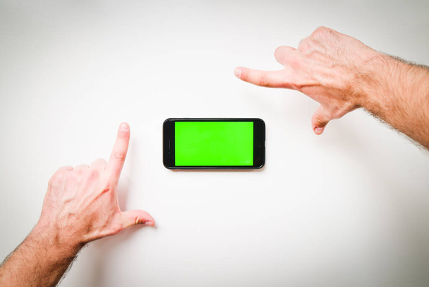 Hände bilden Leerzeichen zum Einfügen von Text oder Design auf grünem Bildschirm mit Smartphone isoliertem weißem Hintergrund - Foto, Bild