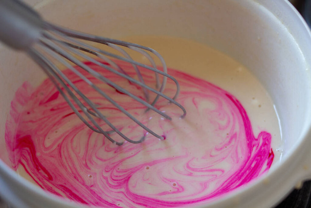 Una frusta da cucina che mescola una sostanza rosa in una ciotola - Foto, immagini