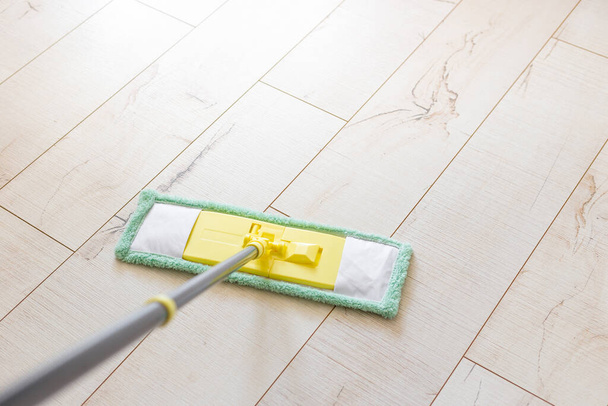 Microfiber yellow mop isolated on white wooden floor background, closeup, indoors - Foto, afbeelding