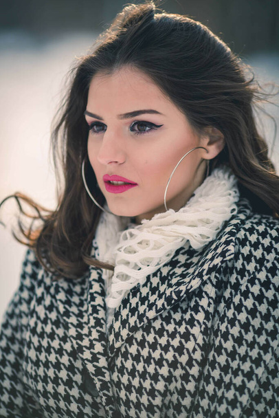 A portrait of a young cute brunette girl in a stylish winter outfit posing outside on a sunny cold day - Foto, Imagem