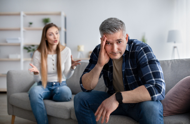 Crisis de la mediana edad y conflictos familiares. hombre maduro sosteniendo su cabeza en el estrés, teniendo lucha con su esposa enojada en casa - Foto, imagen