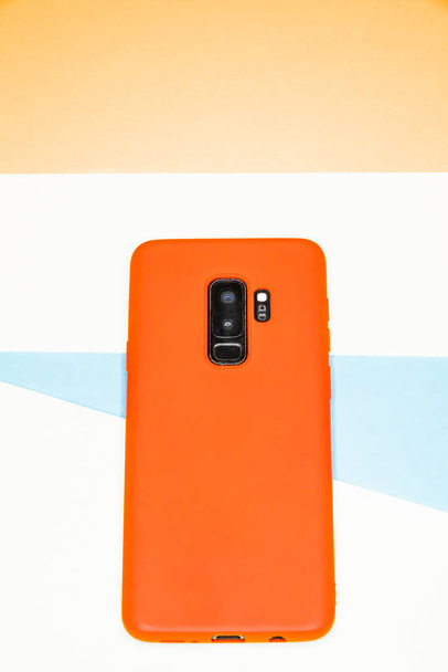 A vertical shot of an orange phone on a colorful paper background - Фото, изображение