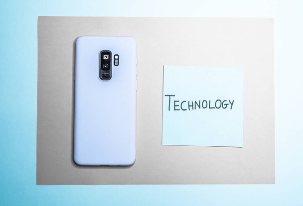A "technology" text and mobile phone in blue case isolated on blue and white background - Fotografie, Obrázek