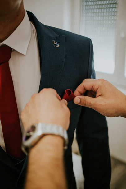 A vertical shot of a man's hands fixing the handkerchief of a groom - 写真・画像