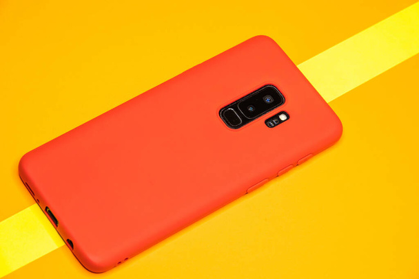 A closeup shot of a red smartphone on a yellow paper surface - Фото, изображение
