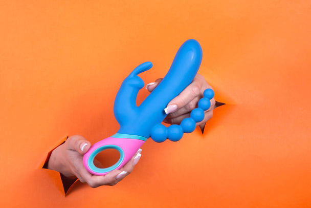 Adult sex toys in women's hands on an orange background. Toys for adult women. - Zdjęcie, obraz