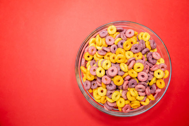 A closeup shot of breakfast cereal rings in a bowl isolated on a bright red background - Fotó, kép