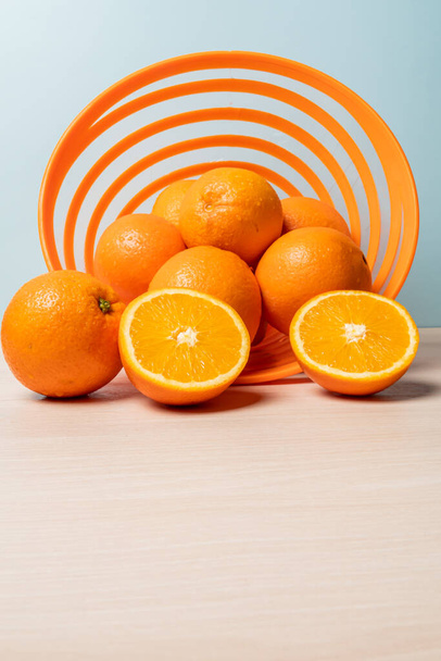 A vertical shot of fresh oranges in a bowl on the table against a blue background - Фото, изображение