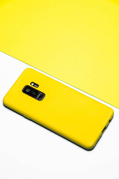 Вертикальный снимок белого смартфона на поверхности желтой бумаги - Фото, изображение