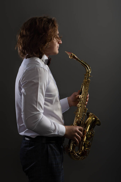Studio portrait of young cool man with saxophone on dark background. - Foto, Imagem