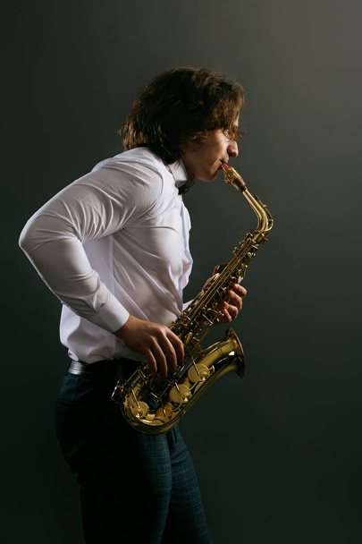 Studio portret van jonge koele man met saxofoon op donkere achtergrond. - Foto, afbeelding