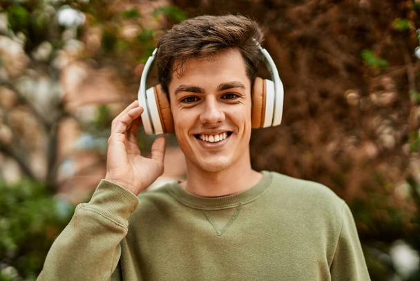 Молодий іспаномовний чоловік посміхається щасливим, використовуючи навушники в місті
. - Фото, зображення