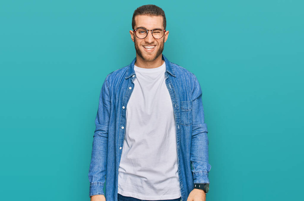 Young caucasian man wearing casual clothes winking looking at the camera with sexy expression, cheerful and happy face.  - Photo, Image