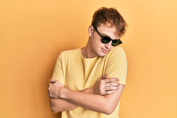 Nuori valkoihoinen mies yllään tyylikäs aurinkolasit halaamalla itseään onnellinen ja positiivinen, hymyillen luottavainen. itserakkaus ja itsehoito  - Valokuva, kuva