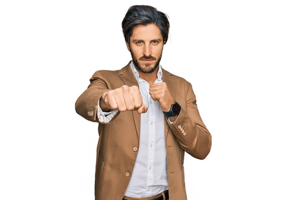 Young hispanic man wearing business clothes punching fist to fight, aggressive and angry attack, threat and violence  - Photo, Image