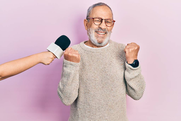 Jóképű, szakállas öregember interjút készít egy riporterrel, aki büszkén sikoltozik a mikrofonjával, ünnepli a győzelmet és a sikert, felemelt karokkal.  - Fotó, kép