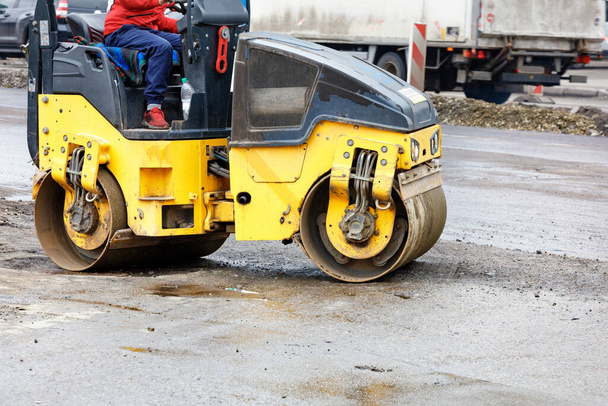 A yellow road roller compacts the base of the roadway at a construction site on a city street. Copy space. - Φωτογραφία, εικόνα