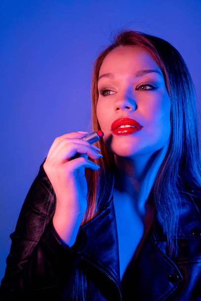 Portrait of a young girl, with long hair, she paints her lips, close-up. Photoshoot in neon light - Фото, изображение
