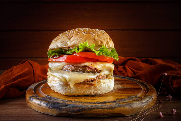 Lahodný hamburger na dřevěném stole, koření a hnědá tkanina - perspektiva a pohled zepředu. - Fotografie, Obrázek