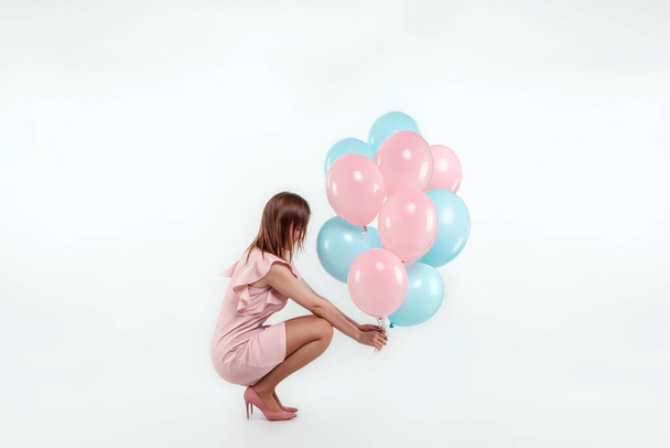 A beautiful young girl sits with blue and pink balloons on a white background. Happiness, spring, holiday - Foto, immagini