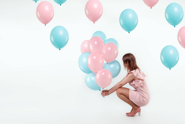 A beautiful young girl sits with blue and pink balloons on a white background. Happiness, spring, holiday - Fotoğraf, Görsel