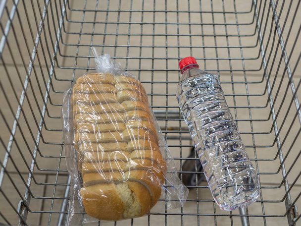Un pain de blé et une petite bouteille d'eau potable dans un panier, panier (chariot). Le concept de pauvreté et de misère. La crise économique mondiale, le boycott du consumérisme. - Photo, image