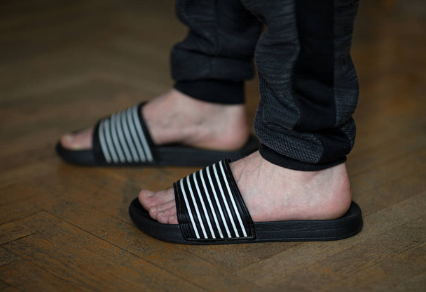 Closeup of male feet in flip flops at home on the wooden floor - Fotografie, Obrázek