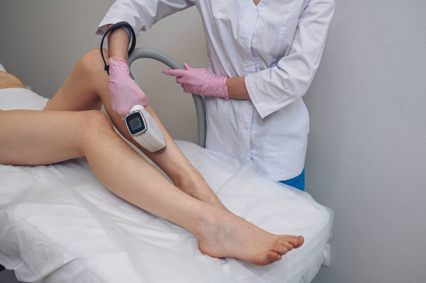 Laser epilation and cosmetology in beauty salon. Hair removal procedure. Laser epilation, cosmetology, spa, and hair removal concept. Beautiful blonde woman getting hair removing on legs - Foto, Imagen