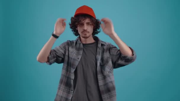 The charismatic young man, energetically puts his cap on his head, looks questioningly forward and then angrily jumps up and breathes his sleeve. isolated over turquoise background.Concept of life - Materiał filmowy, wideo