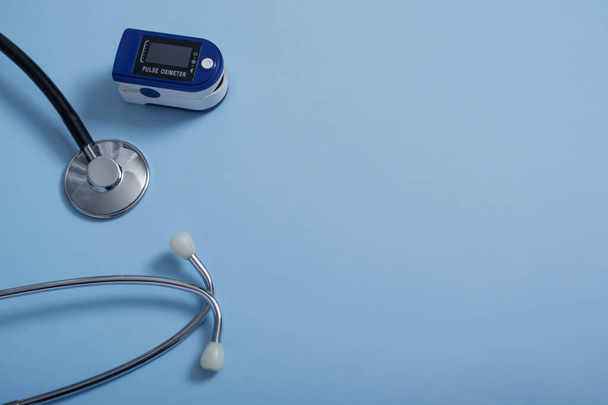 青の背景にパルス酸素濃度計と聴診器を備えたフラット組成心拍数と酸素濃度を測定するために使用されるパルス酸素濃度計. - 写真・画像