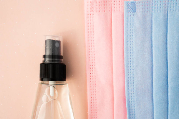 защитные маски для лица и бутылка антисептика для рук на розовом фоне - Фото, изображение