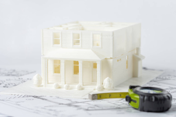 Modello in plastica 3D della casa di famiglia senza tetto stampato su una stampante 3D con filamento bianco con tecnologia FDM per uso architettonico e nastro di misurazione in primo piano. - Foto, immagini