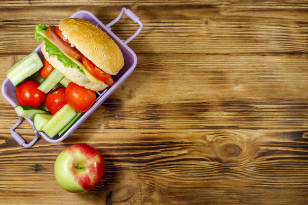 Apple and lunch box with burgers and fresh vegetables on a wooden table. Top view, copy space - Photo, Image