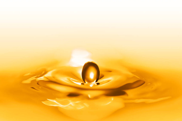 Close up on the splash of a pure beauty lotion droplets falling down on the liquid surface of an elixir of life shining with golden and gilded reflects creating circular waves. - Photo, Image
