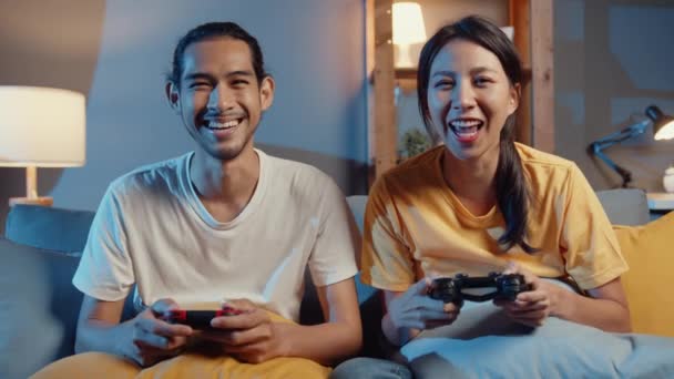 Happy Asia nuori pari mies ja nainen istua sohvalla käyttää joystick ohjain pelata videopeli viettää hauskaa aikaa yhdessä olohuoneessa yöllä. Aasialainen aviopari perhe elämäntapa, Pysy kotona käsite. - Materiaali, video