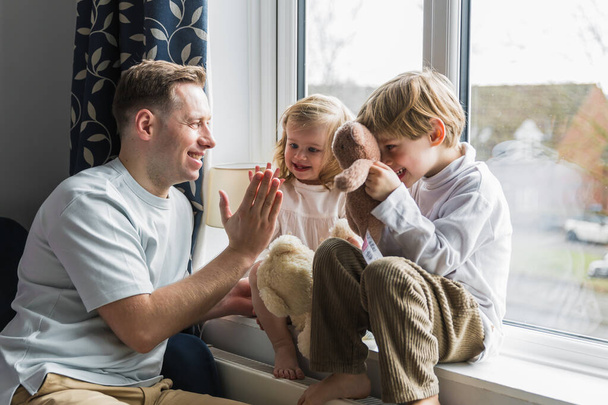 Children sit on the windowsill. Happy dad playing with children. Gives five. A boy and a girl are playing. - Valokuva, kuva