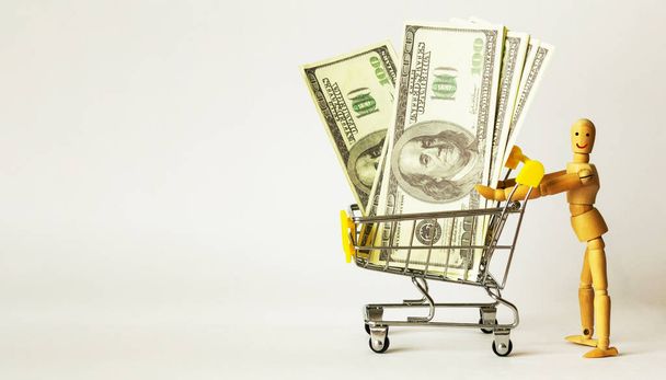Uma boneca de madeira rola dinheiro em um carrinho de compras - Foto, Imagem