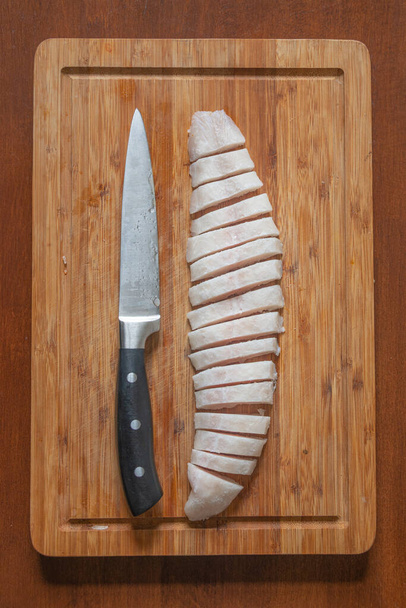 Полузамороженная рыба у деревянной доски, разрезанной на мелкие кусочки большим ножом, детали, крупным планом. Концепция домашней кухни и здорового питания. - Фото, изображение