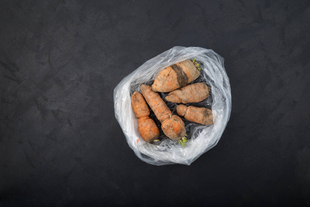 Ugly carrots in plastic bag on dark textured background. Top view, copy space. Improper vegetables storage. Concept - reduction of organic waste. Imperfect products. - Fotoğraf, Görsel