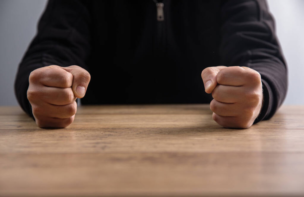 man fists clenched on a wooden tabl - Фото, зображення