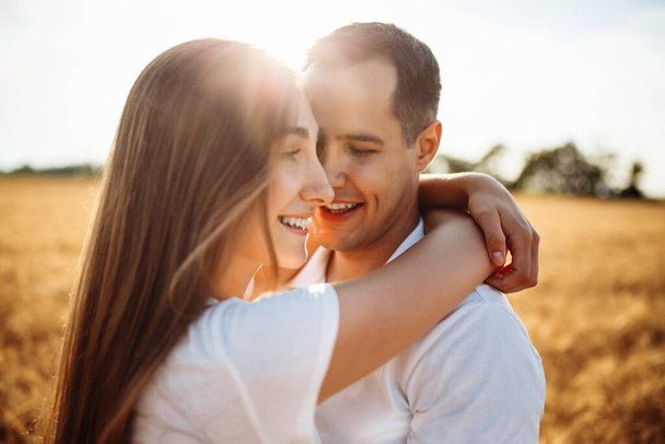 Portret van een gelukkige jongen en meisje op de achtergrond van een rijp veld met tarwe. Een liefdevol koppel dat knuffelt op een zonnige dag. Man en vrouw in de zomer in een tarweveld - Foto, afbeelding