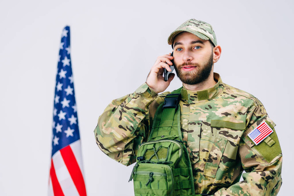 Feliz joven soldado hablando por celular y mirando hacia otro lado. Llama a sus parientes e informa que regresará pronto a casa.. - Foto, Imagen