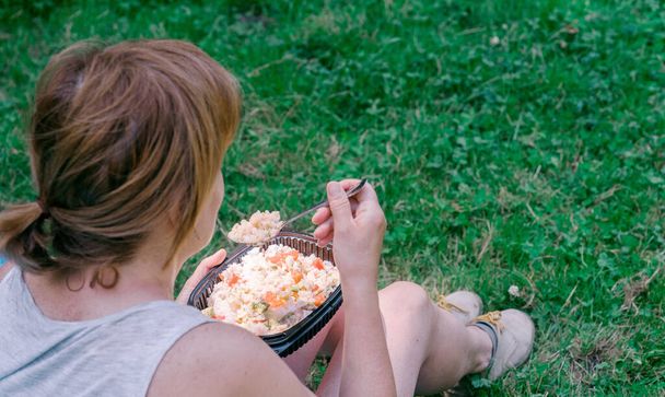Mujer comiendo comida casera preparada en una lonchera de plástico reutilizable en el campo. Vacaciones de verano, comer al aire libre. - Foto, imagen