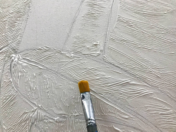 De hand van de kunstenaar schildert met een dun penseel en witte volumetrische verf op het doek. Het creatieve proces van kunst in de kunstschool. - Foto, afbeelding