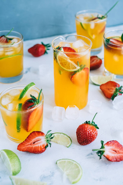 Fresh orange strawberry mojito in different glasses with ice cubes and slices of lime on the table. Summer refreshing drink - 写真・画像