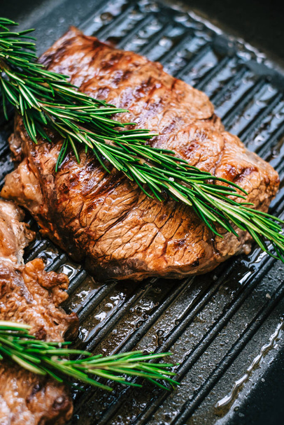 Grilled buffalo beef steak with rosemary in black grill pan on the table, close-up. - Фото, изображение