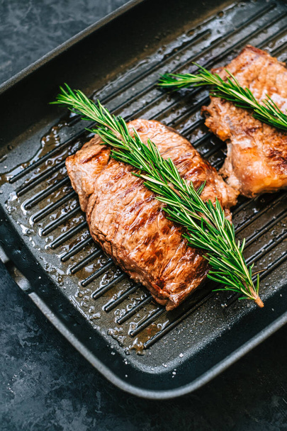 Grilled buffalo beef steak with rosemary in black grill pan on the table, close-up. - Zdjęcie, obraz